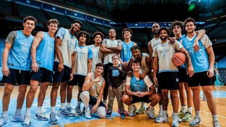 The UNC men's basketball team taking a team photo on the court of the Dean E. Smith Center with a 9-year-old boy, Colburn Dean.