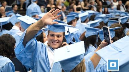 A male student at U.N.C. Chapel Hill Winter Commencement on the phone and waving to someone.