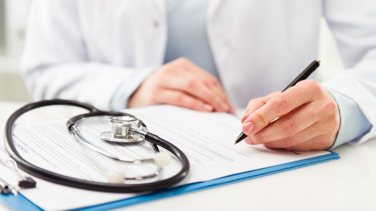 Doctor signing papers. Stethoscope displayed atop papers.